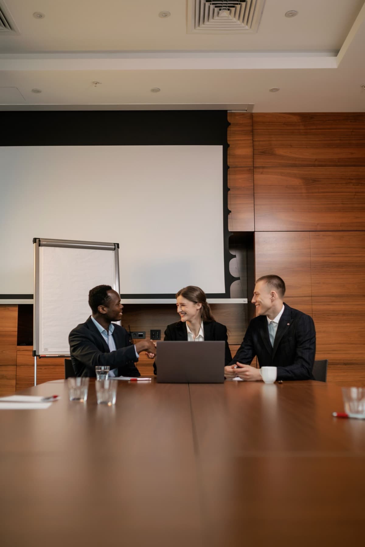 Two professionals shaking hands across a desk after closing a deal